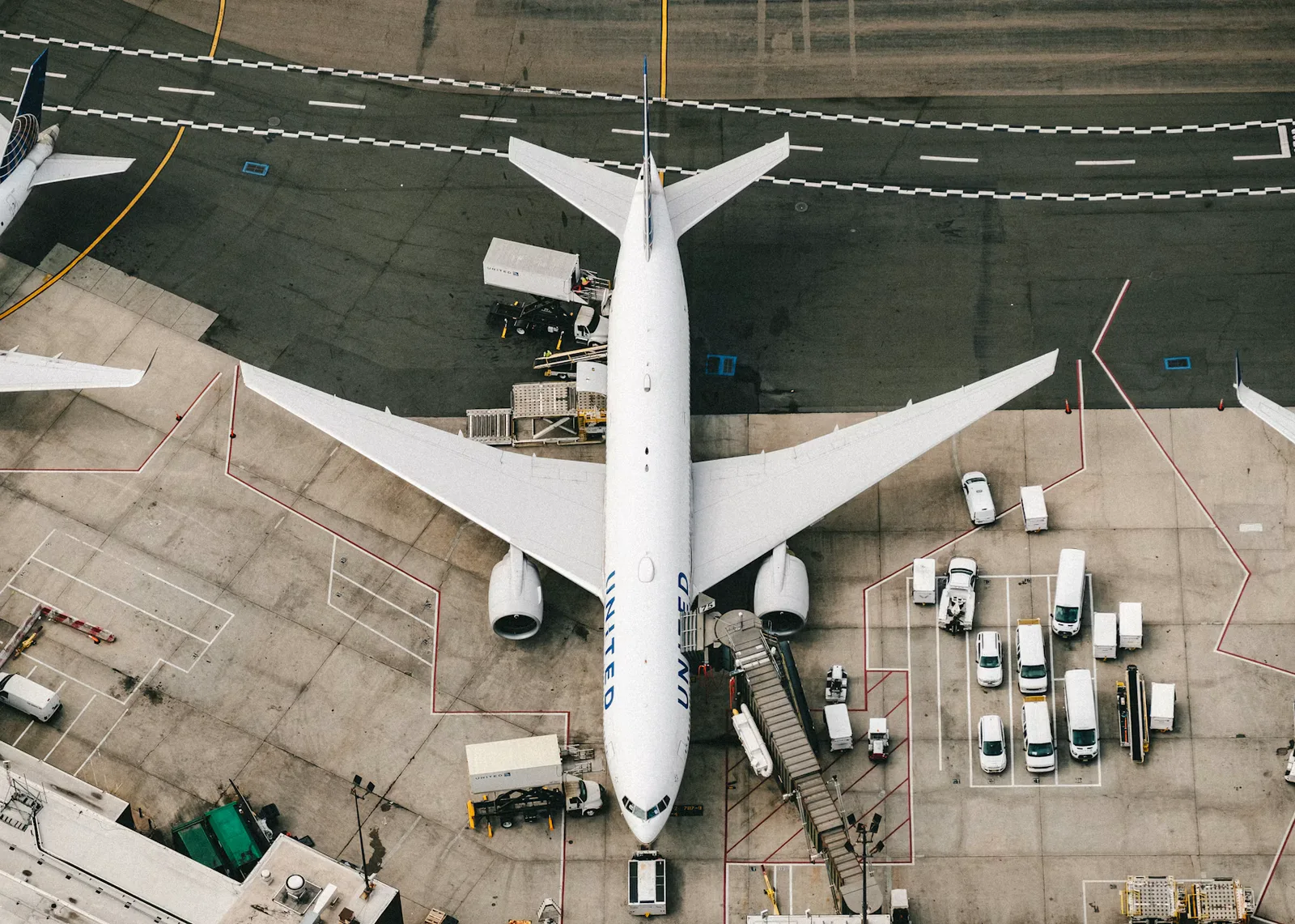 Overhead view of a passenger aircraft and ground vehicles at an airport gate